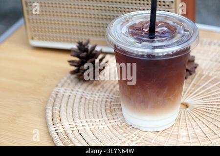 Ein Eiskaffee in einer Plastiktasse sitzt auf einem Holztisch, umgeben von natürlichen Dekorationen Stockfoto