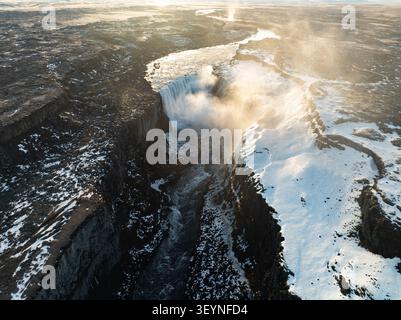 Aus der Vogelperspektive des Dettifoss Wasserfalls, der in einen tiefen Flussschlucht stürzt, umgeben von schneebedeckter Vulkanlandschaft und Nebel unter weichem Licht in Nord Stockfoto
