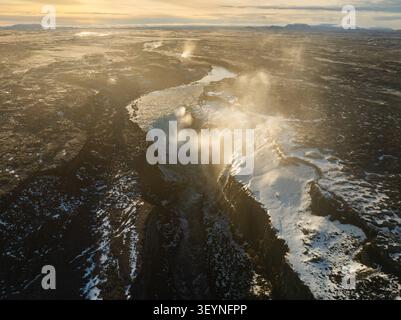 Blick aus der Vogelperspektive auf den Dettifoss-Wasserfall, umgeben von schneebedeckter Vulkanlandschaft und Nebel unter der goldenen Stunde in Nordurthing, Island. Stockfoto