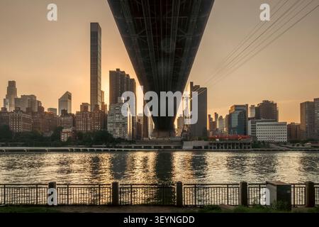 New York, NY - USA - 1. Juli 2026 der Golden Sunset umrahmt die Queensboro Bridge unter den Wänden und führt über den East River in Richtung Manhattans Skyline, wi Stockfoto