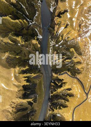 Blick aus der Vogelperspektive auf den Fjadrargljufur Canyon mit moosbedeckten Klippen, einem sich windenden Fluss und Schneeflocken in Skaftarhreppur, Island. Stockfoto