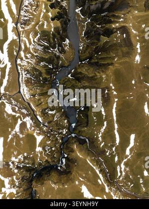 Aus der Vogelperspektive auf den Fjadrargljufur Canyon mit seinem gewundenen Fluss, moosbedeckten Klippen und Schneestücken in Skaftarhreppur, Island. Stockfoto