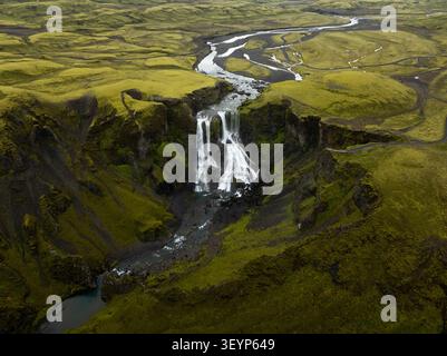 Luftaufnahme des Fagrifoss-Wasserfalls, der in einen tiefen Canyon stürzt, umgeben von einer lebhaften grünen moosigen vulkanischen Landschaft in Kirkjubaejarklaustur, Skaftarh Stockfoto
