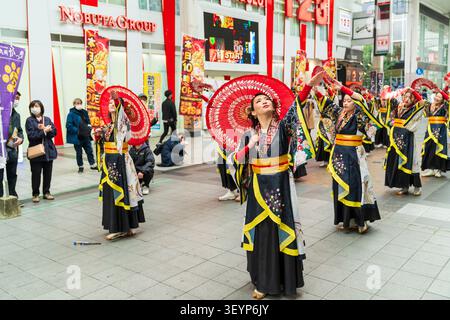 Zwei Reihen lächelnder japanischer junger Tänzerinnen in langärmligen Yukata und mit Regenschirmen und Fans während einer Yosakoi-Tanzveranstaltung in Kumamoto, Japan Stockfoto