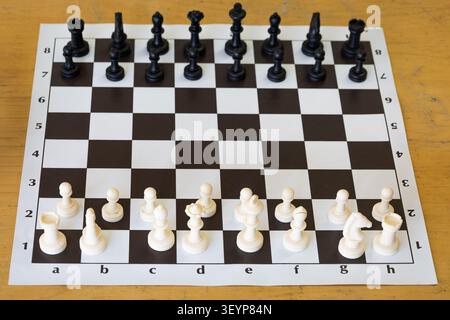 Blick von oben auf ein Schachbrett mit schwarz-weißen Schachfiguren, die in ihren Ausgangspositionen auf einem Holztisch angeordnet sind. Das Bild steht für Strategie, Stockfoto
