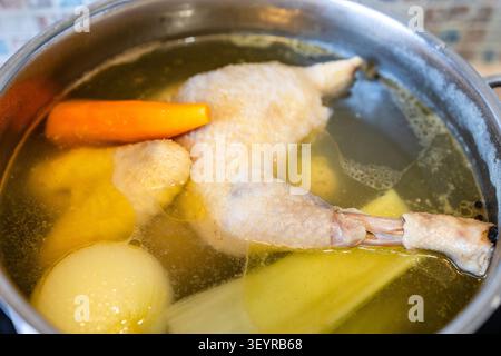 Das ganze Suppe Hühnchen wird in der Küche mit Gemüse in einem Stahltopf gekocht Stockfoto
