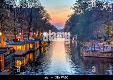Historische Kanalhäuser spiegeln sich in einem Kanal bei Einbruch der Dunkelheit in Amsterdam, Niederlande. Stockfoto