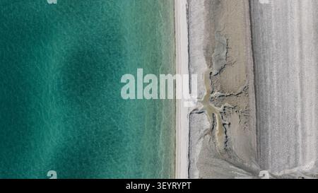 Aus der Vogelperspektive von einer Drohne auf die flussähnlichen Mikrostrukturen, die durch Wasser gebildet werden, das durch den Sand am Ufer des Salda-Sees sickert. Stockfoto