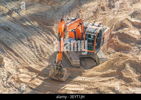 Hellorangefarbener Bagger, der Sand auf der Baustelle ausbaggert, mit robusten Maschinen und breiten Schienen für Stabilität, die sandiges Gelände mit ti Stockfoto