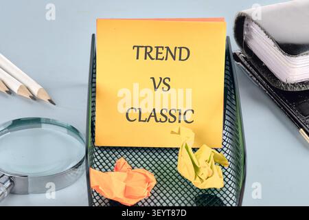 Eine Haftnotiz mit den Worten Trend vs. Classic wird auf einem schwarzen Tablett platziert. Zerknitterte Papiere sind um sie herum, zusammen mit Bleistiften und einer Lupe. Offi Stockfoto