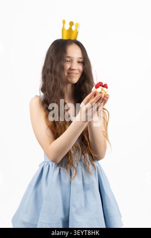 Junge lächelnde Frau, die Krone trägt und Cupcake auf einem professionellen Foto hält... Stockfoto