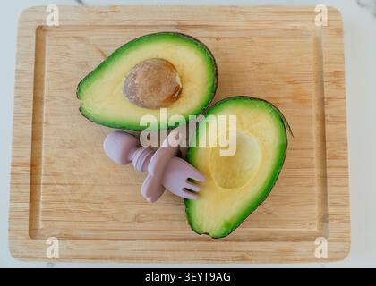 Avocadohälften geschnitten und verzehrfertig auf einem hölzernen Schneidebrett mit einer Plastikgabel, frische und gesunde Lebensmittelzubereitung von oben nach unten, kommerziell Stockfoto