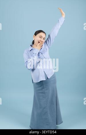 Schwangere Frau, die ihre Arme hoch über dem Kopf in Atelier mit Blau streckt Stockfoto