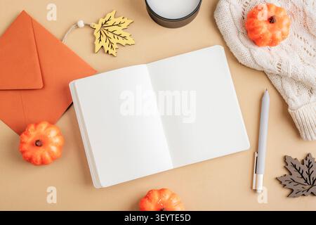 Offenes leeres Notizbuch mit Herbstdekorationen, Kürbissen, Kerzen und kuscheliger Pullover. Saisonale Komposition mit Kopierraum, flach liegend. Stockfoto