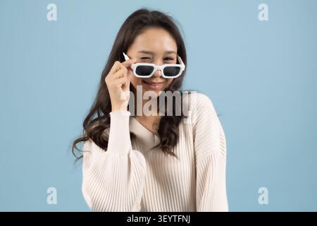 Frau mit Sonnenbrille und verspielt im Studio mit blauem Hintergrund Stockfoto