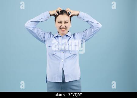 Frau, die Hände auf dem Kopf hält, sieht schockiert oder verärgert im Studio mit Blau aus Stockfoto