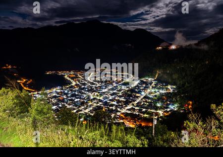 Atemberaubender Hochwinkelblick auf die beleuchtete Stadt Banos de Agua Santa, eingebettet in ein Bergtal bei Nacht in Ecuador. Stockfoto