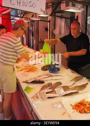 Venedig, Italien - 30. Mai 2026: Fischhändler in schwarzem Hemd, der ältere Kunden an der Fischtheke mit frischem Fisch serviert Stockfoto