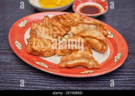Authentische asiatische gedämpfte und knusprig gebratene Knödel, serviert mit Dip-Sauce und gelbem Rettich auf einem dunklen Holztisch. Stockfoto