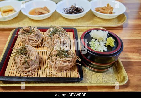 Gekühlte Buchweizennudeln auf einer Bambusmatte mit herzhafter Dip-Sauce. Essstäbchen heben einen Bissen, der eine erfrischende authentische asiatische Sommer Mahlzeit einfängt. Stockfoto