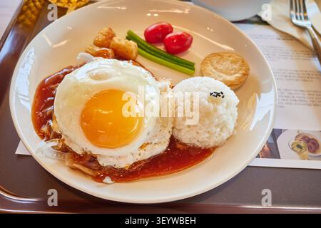 Fleischpastete mit süßer Sauce, einem Spiegelei, Reis und frischem Gemüse auf einem weißen Teller. Eine herzhafte und köstliche Café-Mahlzeit. Stockfoto
