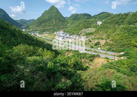 Moderner Schnellweg, der durch ein ländliches Karstbergdorf in Qiannan, Guizhou, China führt Stockfoto