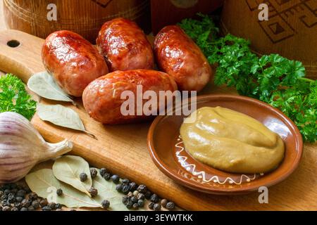 Frittierte Fleischwürste mit Senf. Würstchen mit Gewürzen und Kräutern auf einem hölzernen Schneidebrett. Stockfoto