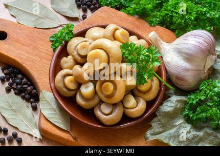 Marinierte Champignonpilze. Pilze mit Kräutern und Gewürzen. Champignons in Dosen auf einem Teller. Pilze mit Petersilie, Knoblauch, Lorbeerblatt und Pfeffer Stockfoto