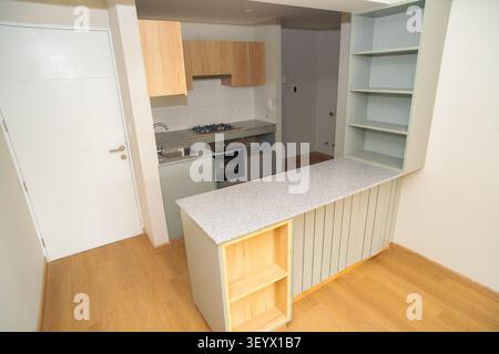 Moderne kleine Küche mit Inselarbeitsplatte, Holzschränken und offenen Regalen in einer neuen Wohnung Stockfoto