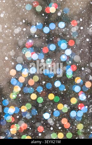 Vertikaler Weihnachtshintergrund mit kleineren warmen Bokeh-Lichtern und der sanften Kontur eines dekorierten Weihnachtsbaums in gemütlicher Atmosphäre. Fallender Schnee A Stockfoto