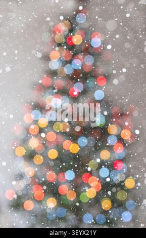 Vertikaler Feiertagshintergrund mit warmem leuchtendem Weihnachtsbaum-Bokeh mit einer deutlich sichtbaren Baumumrandung auf einem hellen weißen Hintergrund. Sanftes Herunterfallen Stockfoto