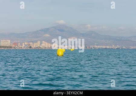 Eine führende Linie von leuchtend gelben Boje, die auf dem ruhigen Meer in der Bucht von San Juan, Alicante, Costa Blanca schwimmt Stockfoto