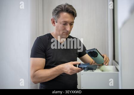 Konzentrierter Mann, der einen Kauf bezahlt, indem er sein Smartphone in die Nähe eines Zahlungsterminals hält. Mobile Wallet, NFC-Transaktion und digitaler Handel. Stockfoto