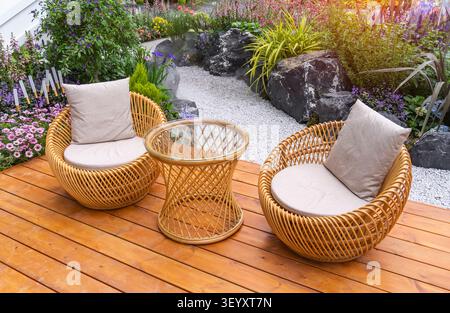 Der Garten ist mit Korbmöbeln im Freien und Blumen in Töpfen dekoriert. Frisch blühende Topfpflanzen für Sommerunterhaltung Stockfoto