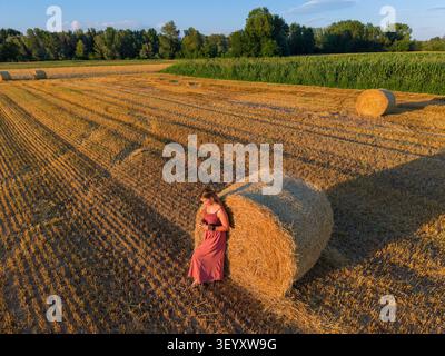 Luftaufnahme einer jungen Frau, die neben Heuballen in einem abgeernteten Weizenfeld spaziert Stockfoto