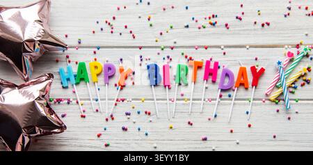 Text Happy Birthday by Kerzenbriefe mit Geburtstagsasseccories, Kerzen und Konfetti auf weißem hölzernem Hintergrund Stockfoto