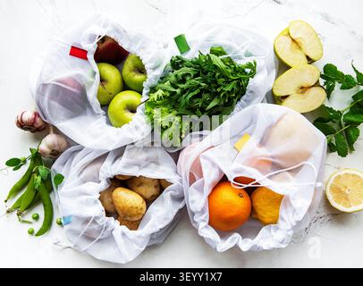 Obst und Sommergemüse in wiederverwendbaren, umweltfreundlichen Netztüten auf Marmorboden. Kein Verschwendung einkaufen. Ökologisches Konzept. Stockfoto