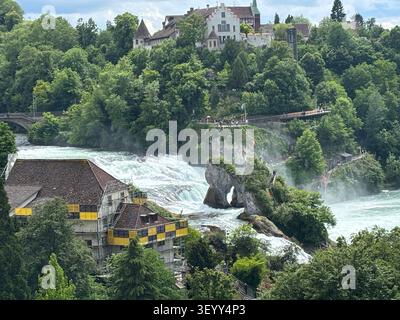 Hohe Blickwinkelansicht der massiven Rheinfälle, die um Felsformationen tosen, mit Schloss Laufen auf dem Hügel Stockfoto