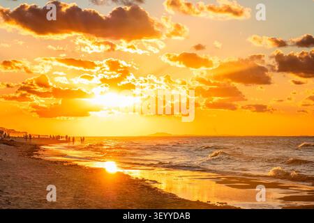 Wunderschöner Sonnenuntergang über dem Strand mit lebhaften Menschen, die den Abendspaziergang am Meer genießen. Stockfoto