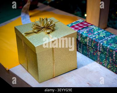 Wunderschön verpackte Weihnachtsgeschenke mit einer glitzernden goldenen Geschenkbox mit Schleife und einem gemusterten grünen Geschenk auf einer Holzoberfläche Stockfoto