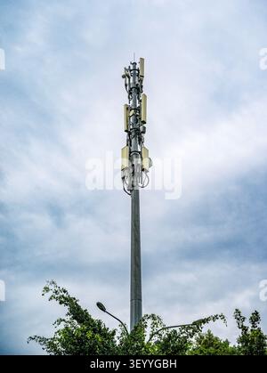 Flacher Winkel eines hohen Telekommunikations-Mobilfunkturms mit mehreren Transceiver-Antennen vor bewölktem Himmel Stockfoto