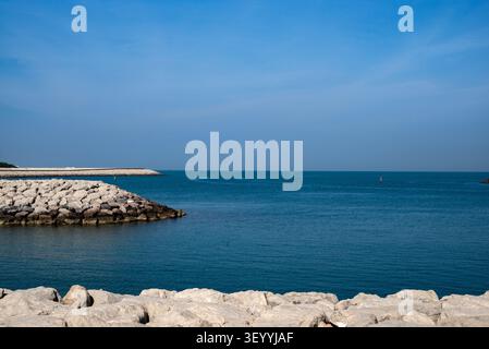 Horizontale Breitaufnahme einer tiefblauen Meeresbucht, eingerahmt von Steinmolen und Felsverbauungen unter einem klaren blauen Himmel, Dubai Stockfoto