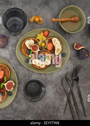 Frühstückstisch mit Pfannkuchen mit Feigen, Beeren, Bananenscheiben und Honig Stockfoto