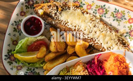 Gebackene Forelle mit geschmolzenem Käse, Kartoffelkeilen und frischem Gemüsesalat Stockfoto