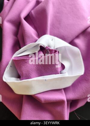 Näharbeiter kleben vor dem Nähen auf der Nähmaschine weiße Verkleidung an lila Strickmaterial, Details zur Bekleidungsproduktion. Industrie, Kunst Stockfoto