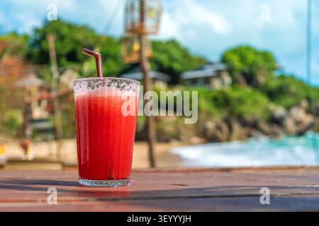 Erfrischendes Getränk aus roter Wassermelone im Glas mit einem Strohhalm auf Holztisch im Strandcafé am Meer, Samui Island, Thailand. Kalter tropischer Obst-Smoothie Stockfoto