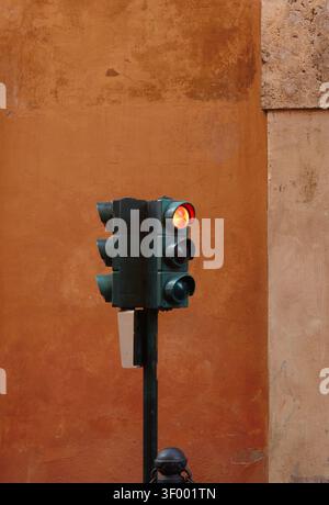 Eine Vintage-Ampel zeigt ein rotes Signal, das an einer Stange montiert ist und an einer verwitterten orangen Wand angebracht ist und die farbigen Linsen und das urbane Set des Lichts hervorhebt Stockfoto