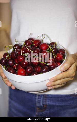Eine Nahaufnahme einer Frau, die ein weißes T-Shirt und eine blaue Jeans trägt und eine große, volle weiße Keramikschale hält, die reichlich mit frischem, Stockfoto