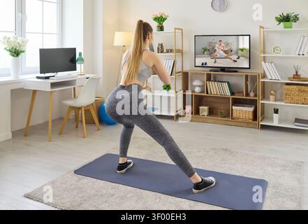 Frau macht Heimtraining nach Online-Training im Fernsehen und dehnt sich auf Yogamatte Stockfoto