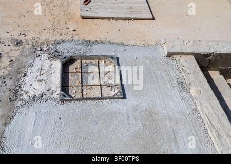 Auf einer Baustelle ist ein quadratisches Metallgitter sichtbar, umgeben von frisch gegossenem Beton und Kies Stockfoto